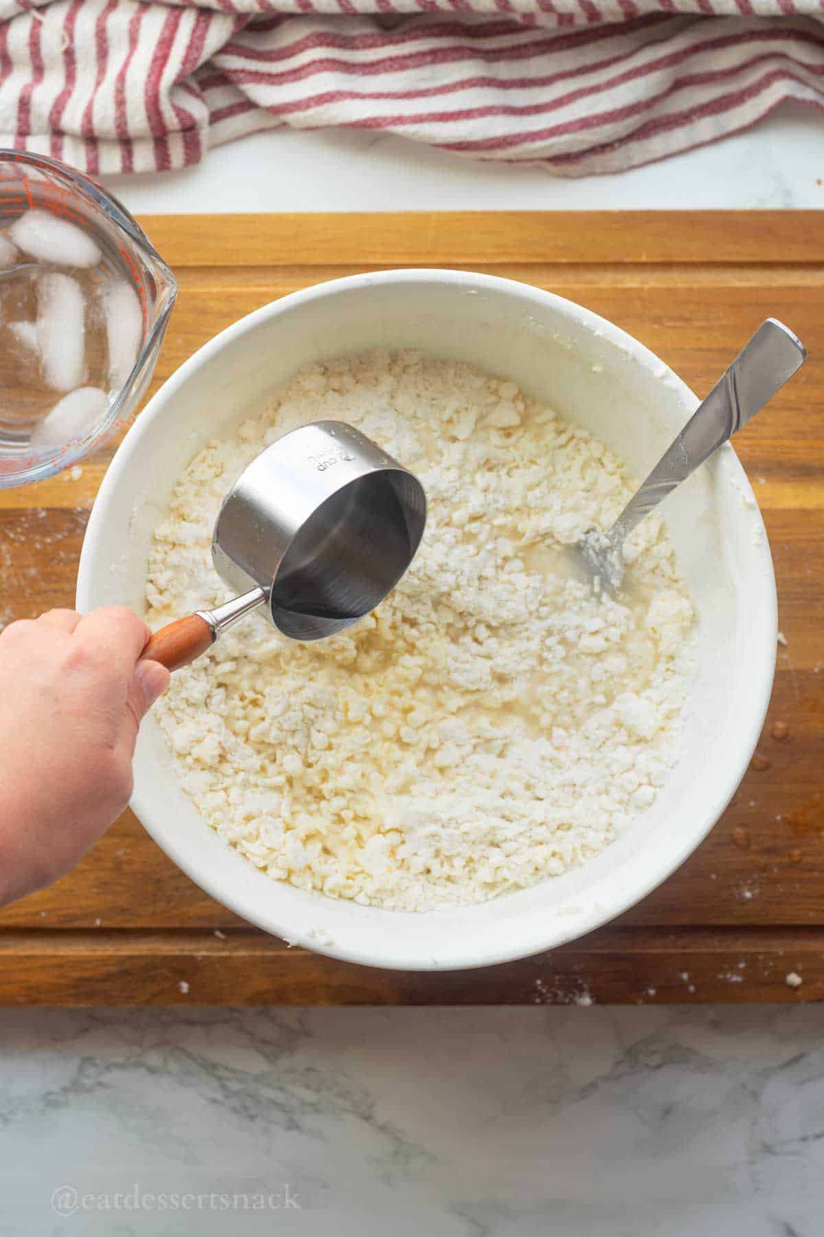 Pouring cold water into bowl of pie crust dry ingredients.