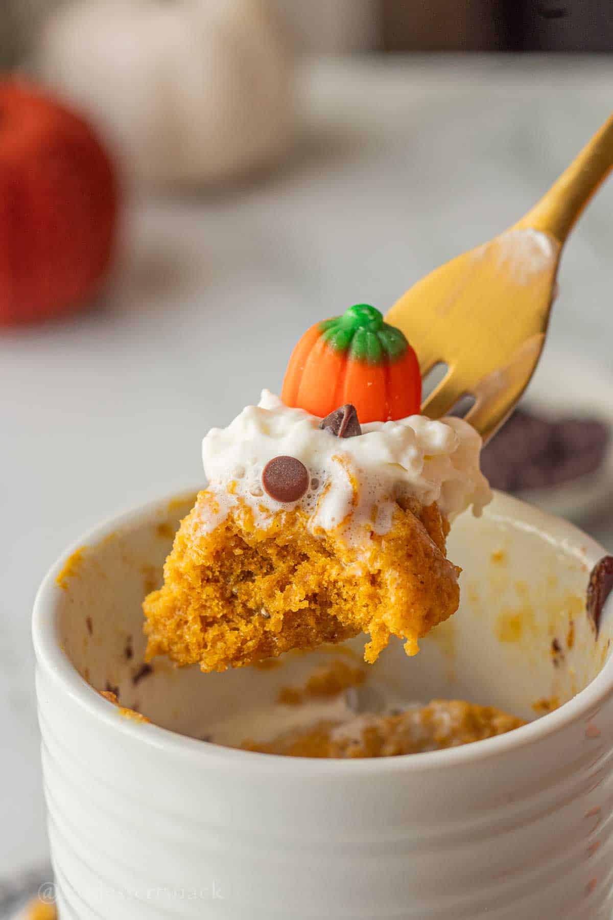Bite of spiced pumpkin mug cake on gold fork above mug.
