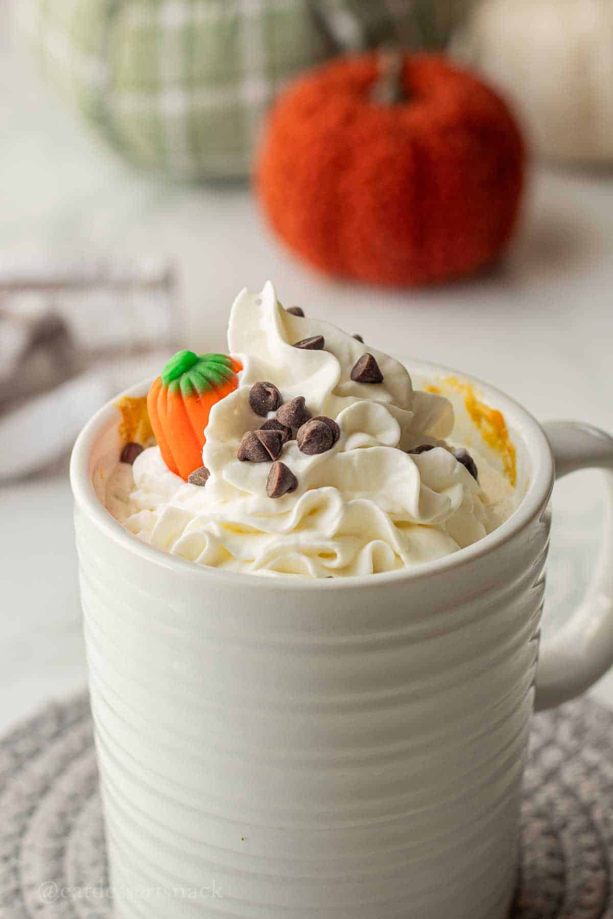 Whipped cream and pumpkin candy on top of cooked pumpkin spice mug cake.