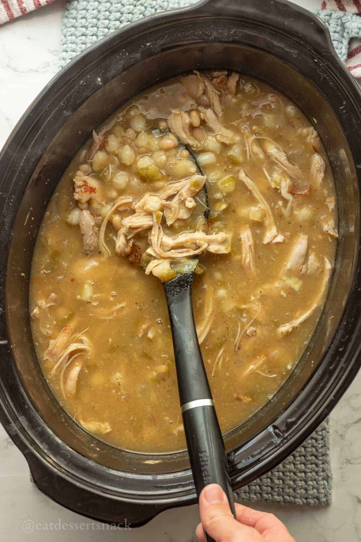 Shredded chicken in crockpot of posole with serving spoon.