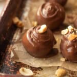 Dipped peanut butter ball with peanut on top on pan.