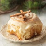 Eggnog cinnamon roll on white plate with cinnamon sticks.