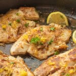 Cooked tilapia with lemon zest and parsley in pan.