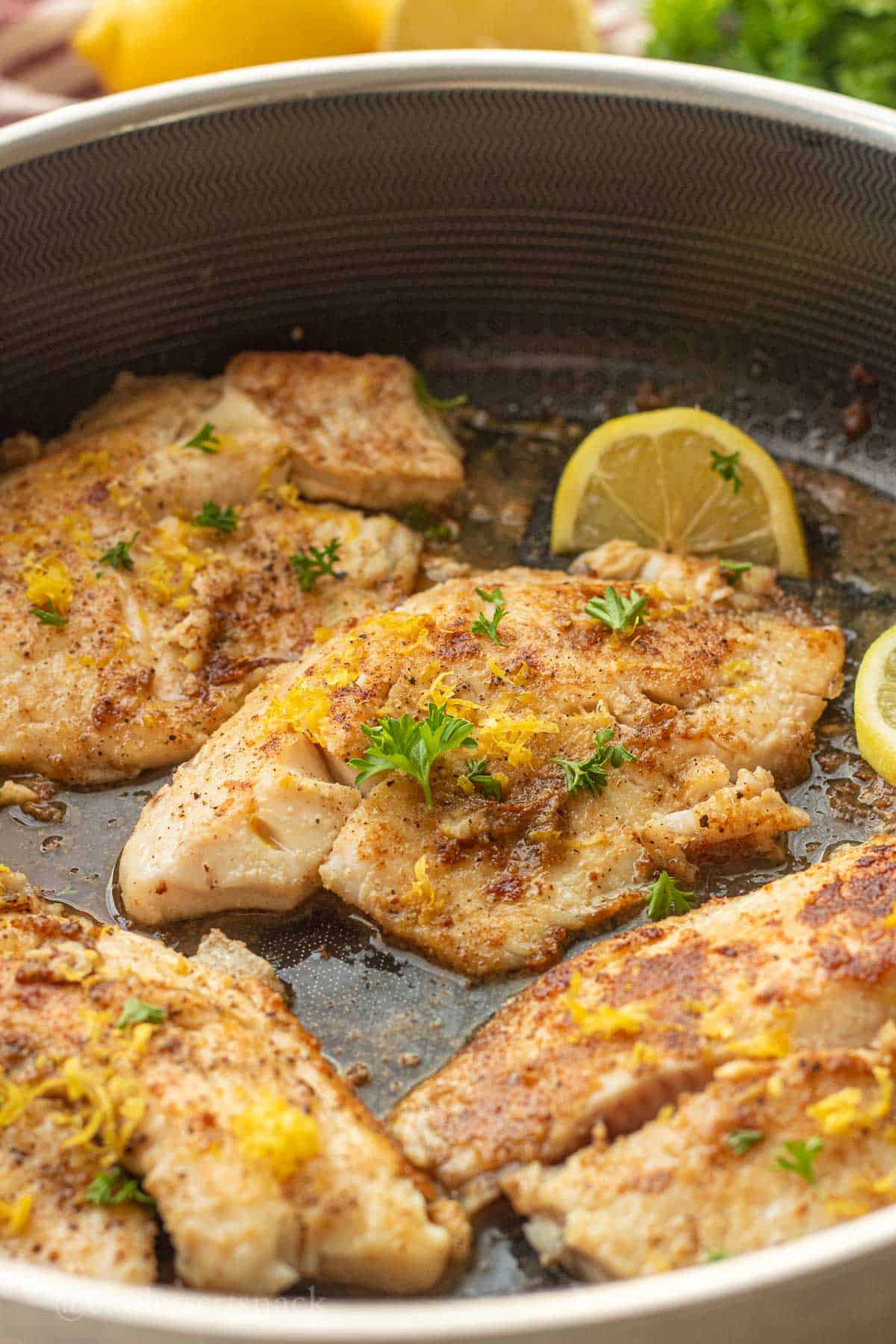 Cooked tilapia with lemon zest and parsley in pan.