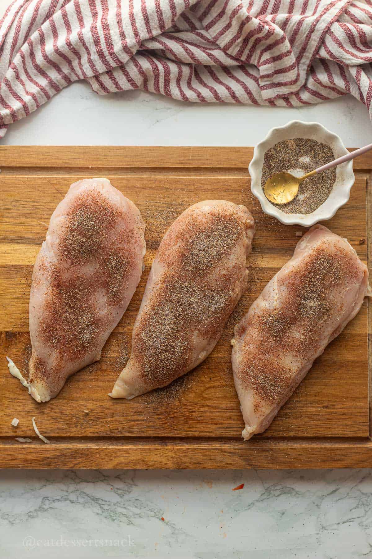 Seasoning on chicken breasts on wooden cutting board.