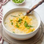Bowl of cooked cauliflower leek potato soup on plate with wooden spoon.