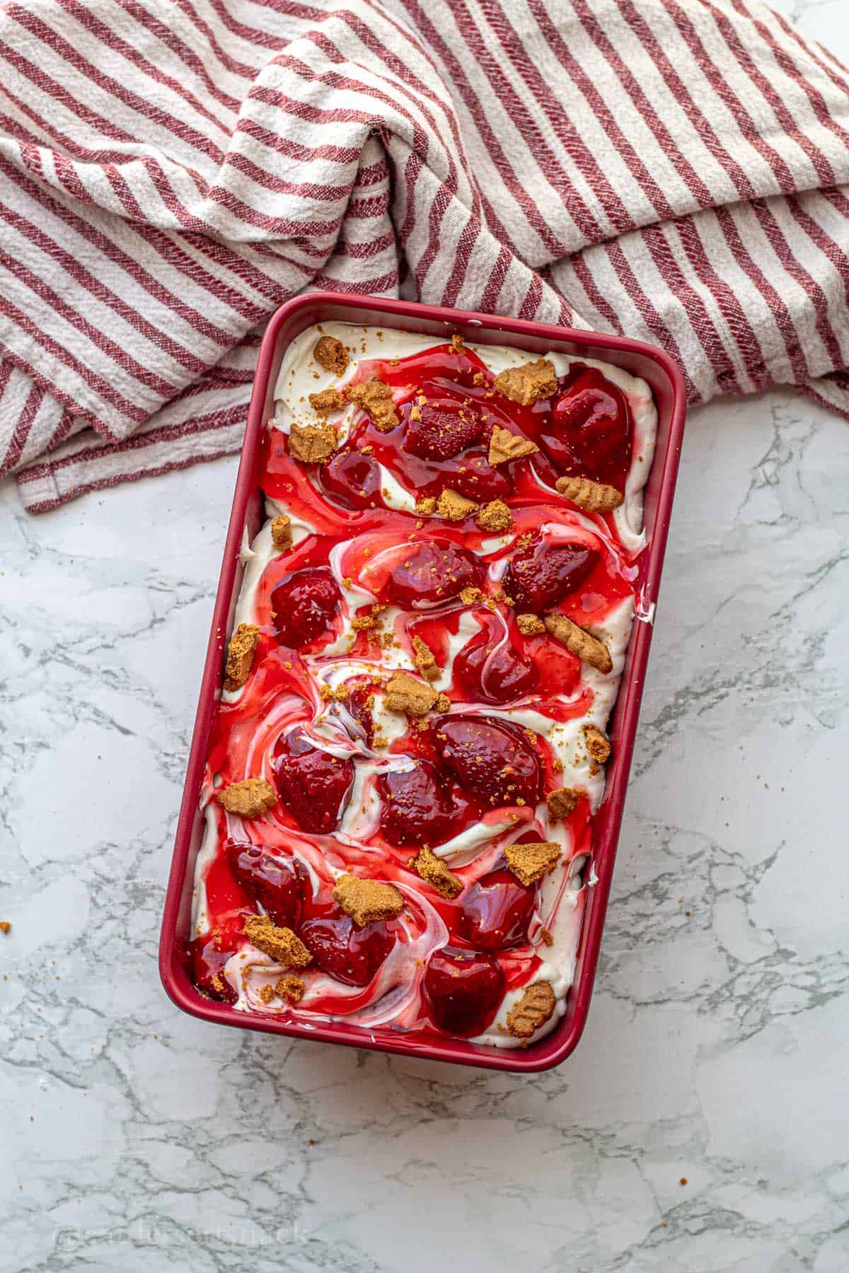 Strawberry cheesecake ice cream in a pan with biscoff crumbles on top.