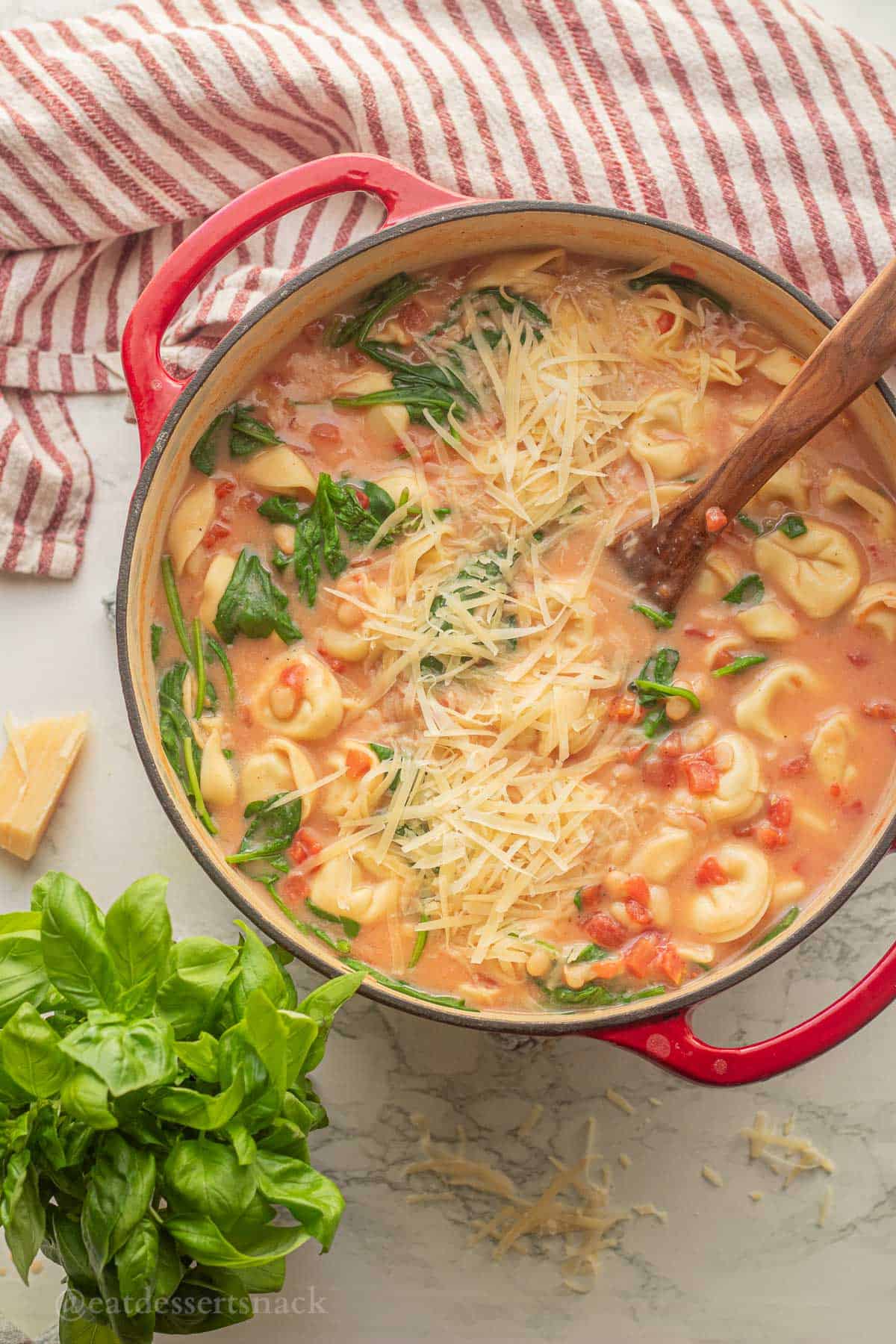 Tortellini tomato soup in pot with wooden spoon and basil.