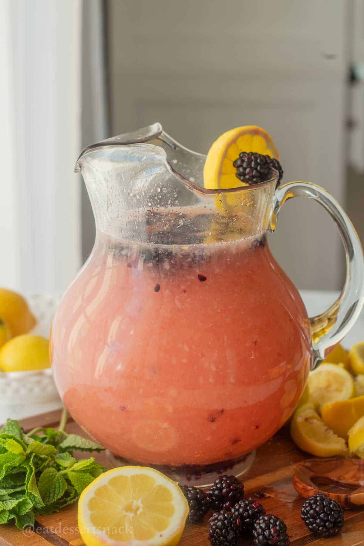 Full pitcher of lemonade with lemon slice and blackberry on rim.