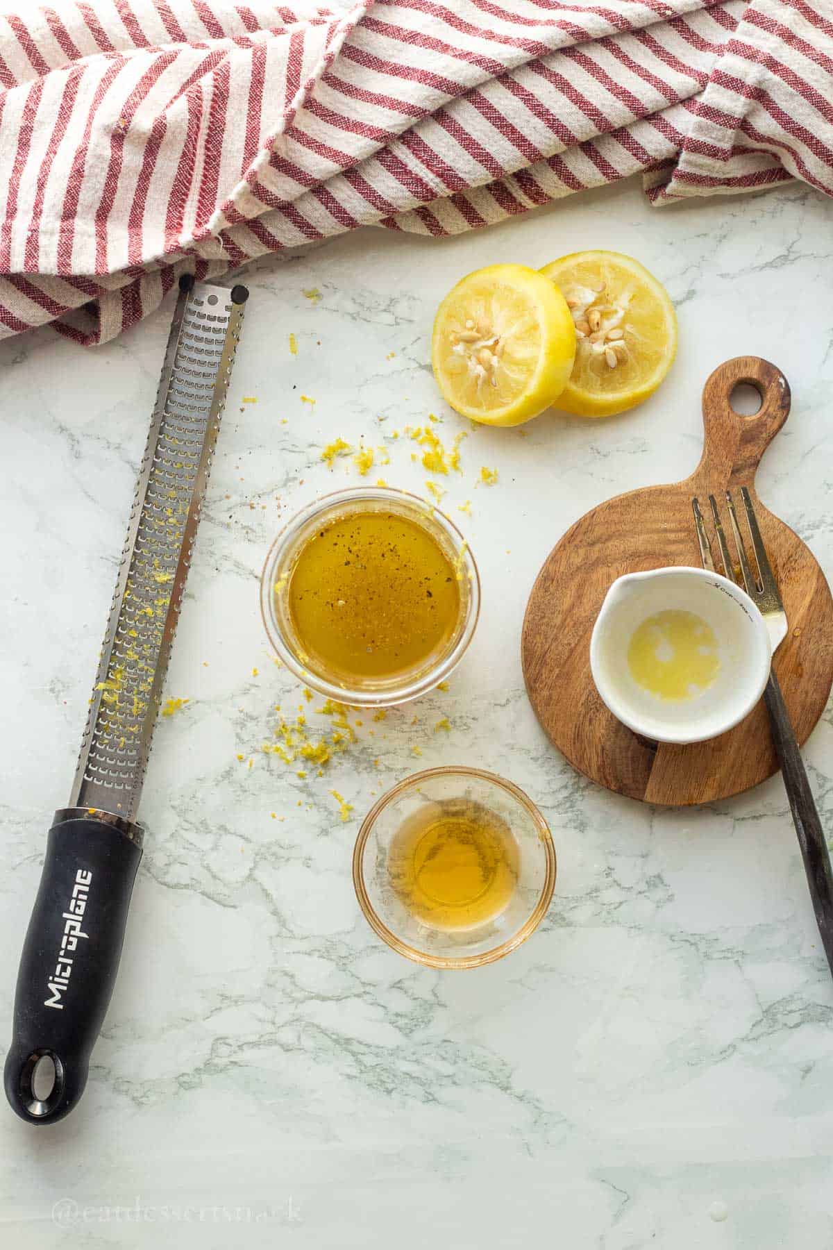 Olive oil, lemon, honey, salt and pepper in bowls on marble.