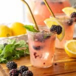 Glass of blackberry pear lemonade on wood board with straw.