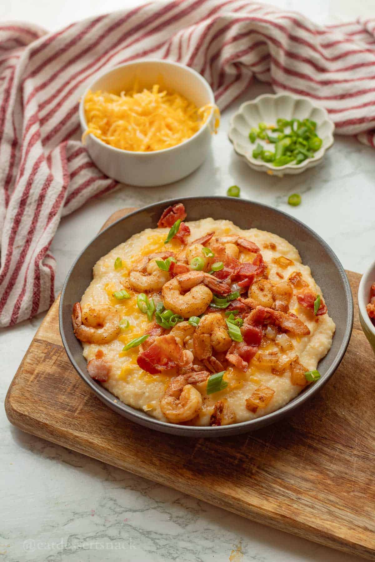 Plated cheesy shrimp and grits with bowl of cheese on the side.