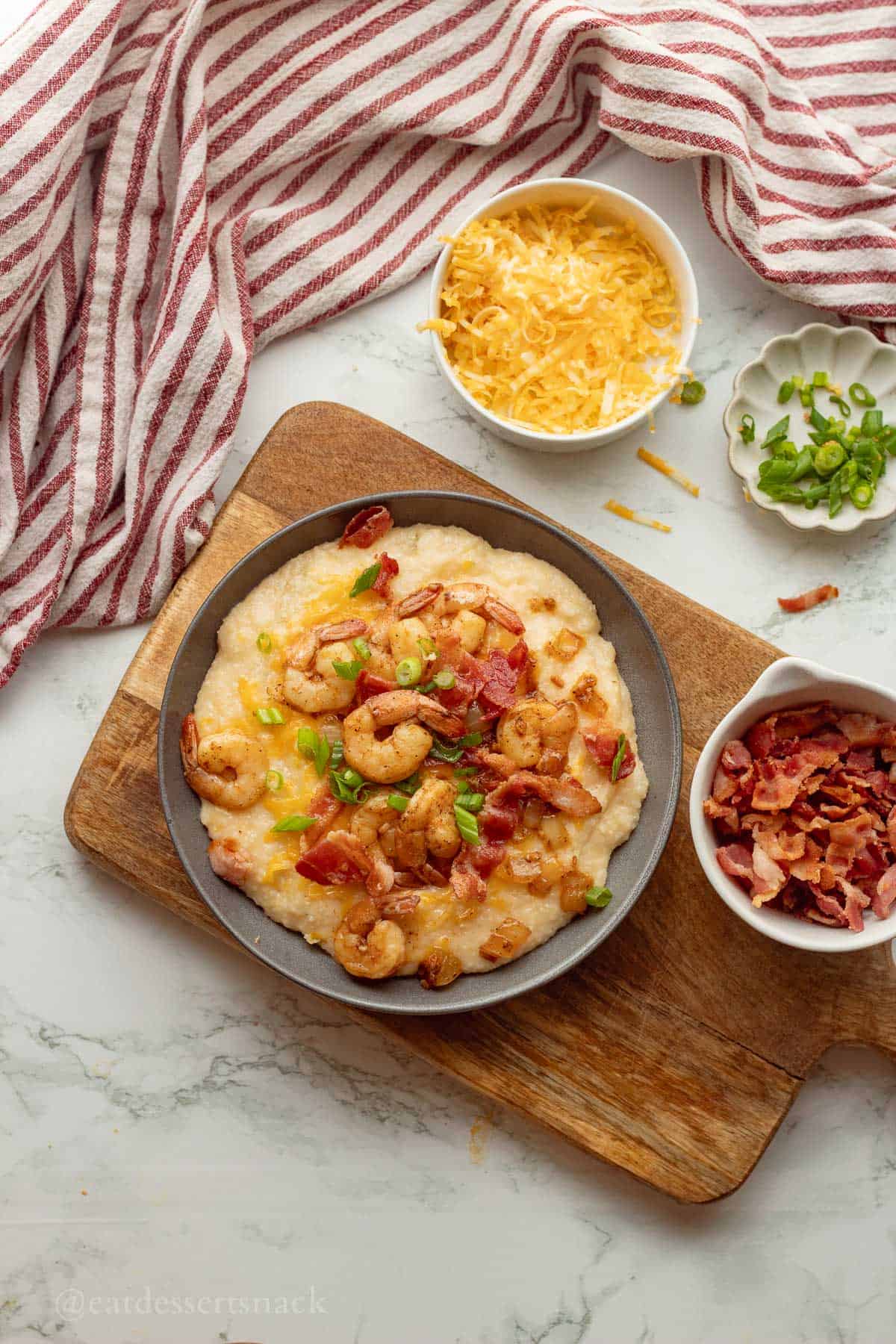 Plated cheesy shrimp and grits with bowl of bacon on the side.
