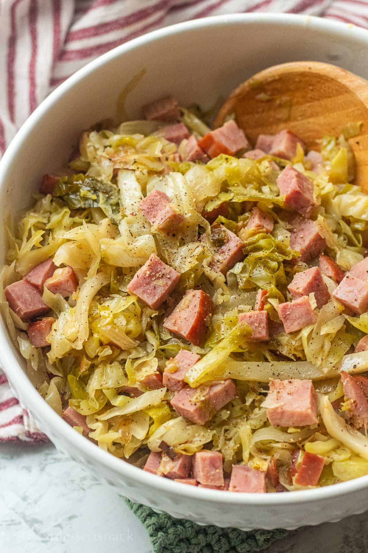 Cooked cabbage and ham in bowl with spoon.