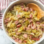 Cooked cabbage and ham in bowl with spoon.