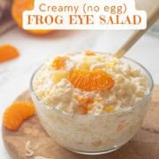 Frog eye salad in glass bowl with gold spoon on cutting board.