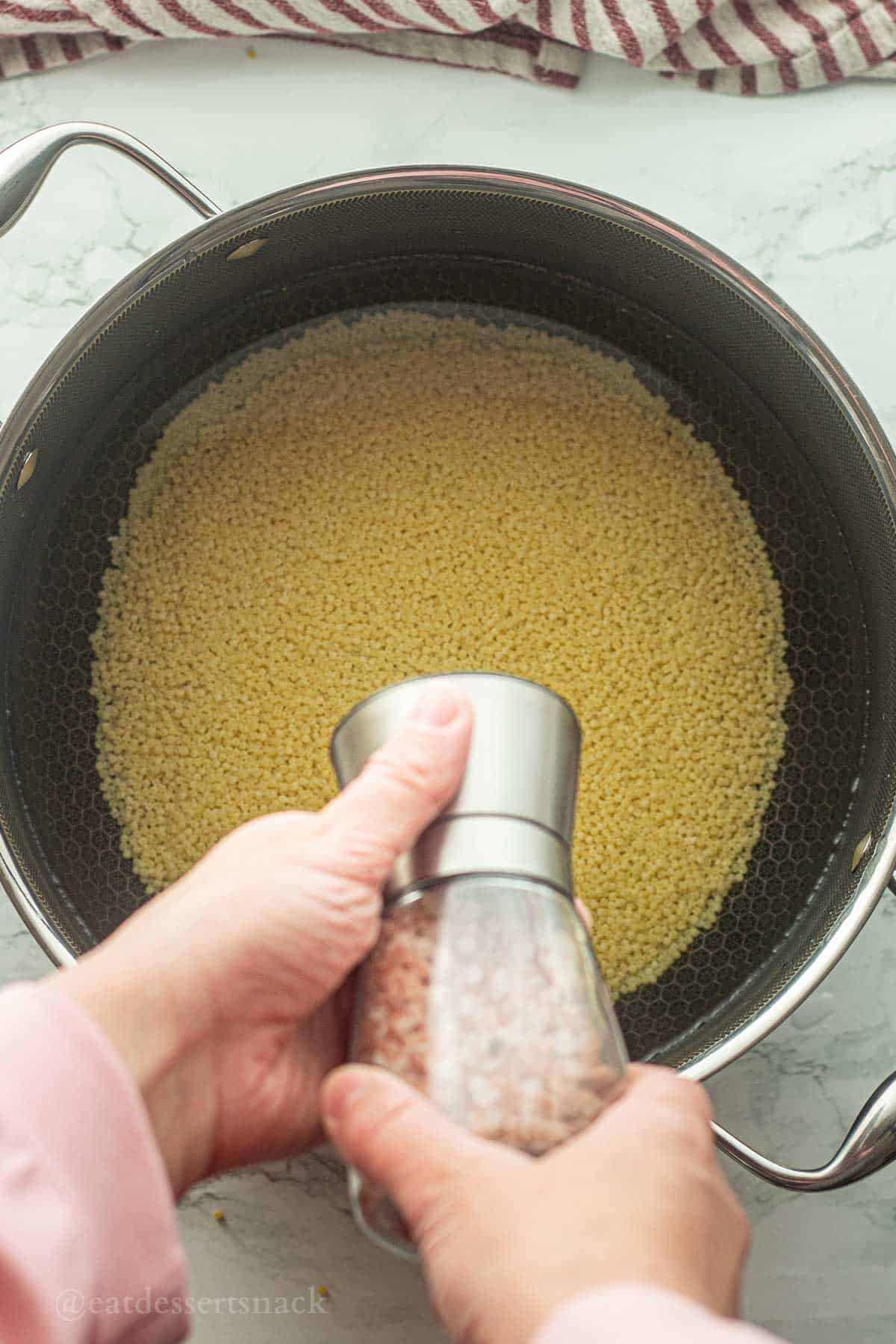 Salt shaker above pot of uncooked acini de pepe noodles.