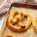Baked soft pretzel on parchment paper in pan.
