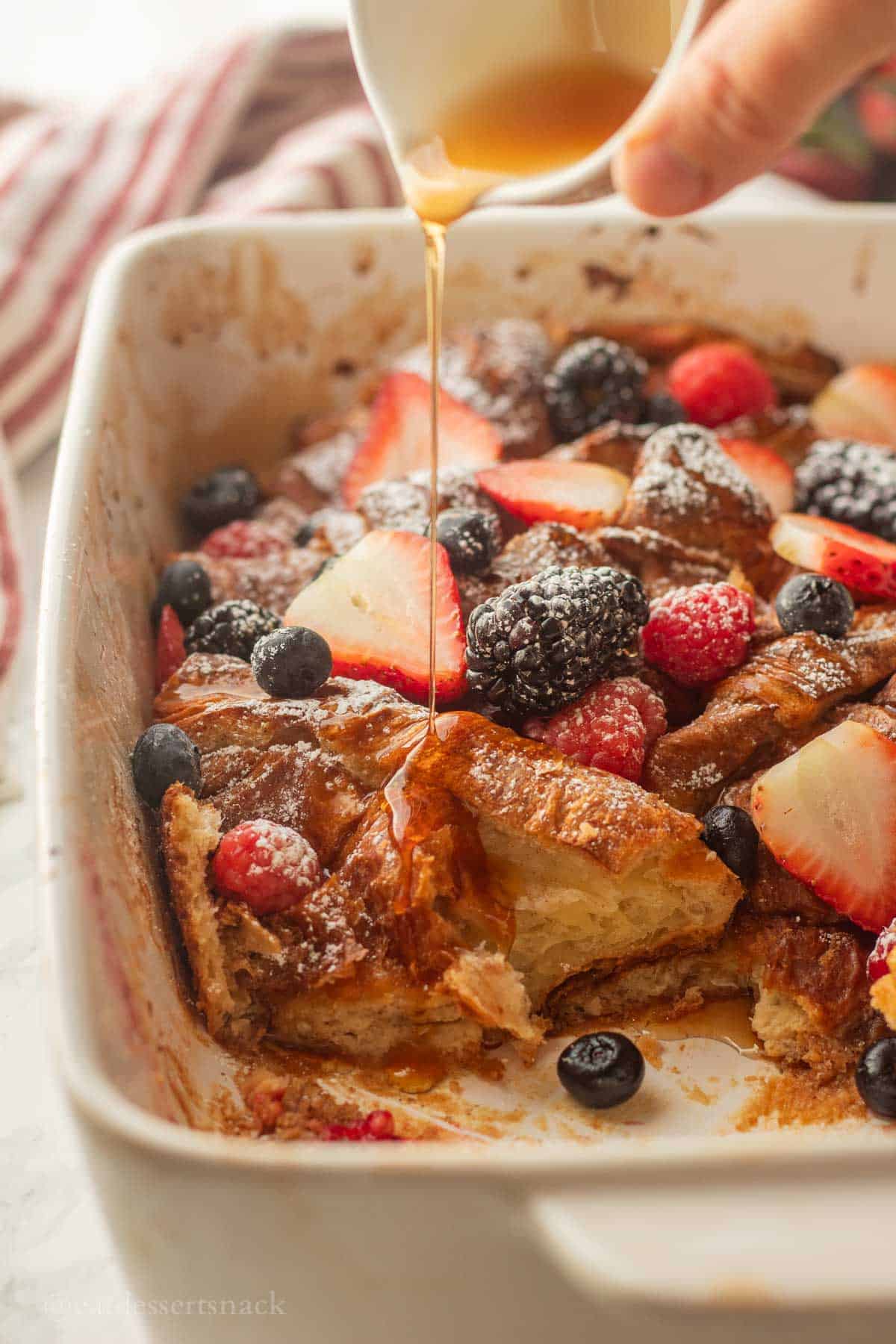 Pouring syrup over baked french toast croissants in pan.