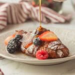 Pouring syrup over baked croissant slice on plate.