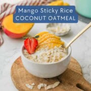Bowl of mango coconut oatmeal on wood cutting board with gold spoon.