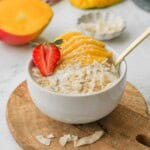 Bowl of mango coconut oatmeal on wood cutting board with gold spoon.