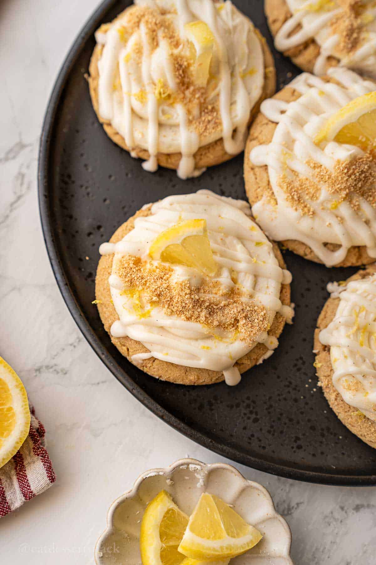 Graham cracker crumbs sprinkled over frosted lemon cheesecake cookies on plate.